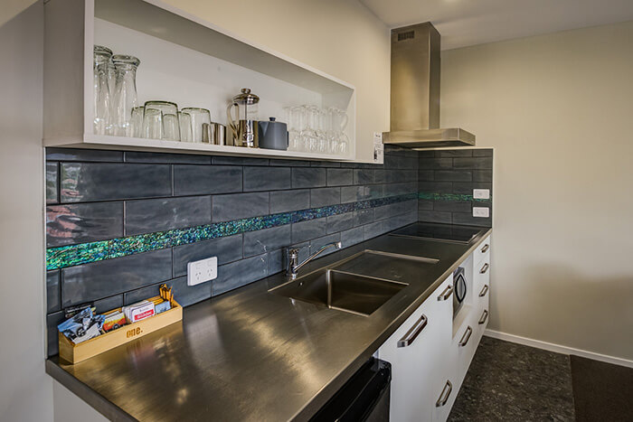 Premium one-bedroom apartment's modern kitchen with white joinery and stainless steel benchtops and appliances.